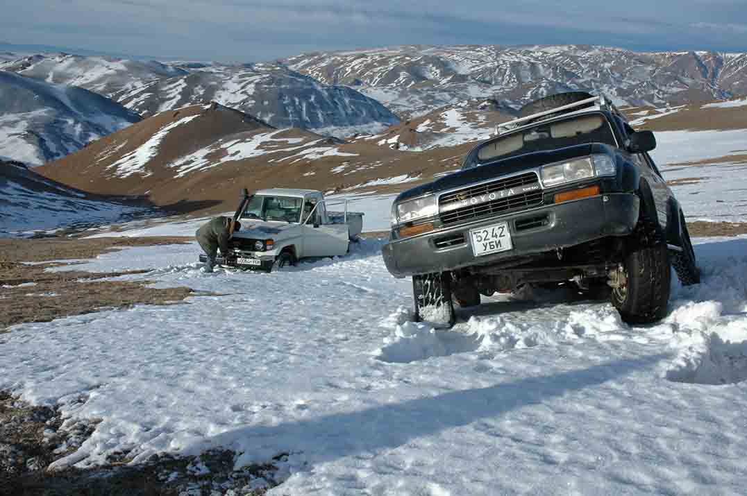 Mongolia- on top of a mountain, one vehicle stuck in snow, the other with engine issues.