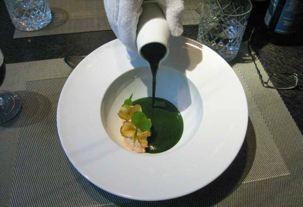 A gloved-hand pours the Nettle soup with Karelian trout sorbet and willow-tea